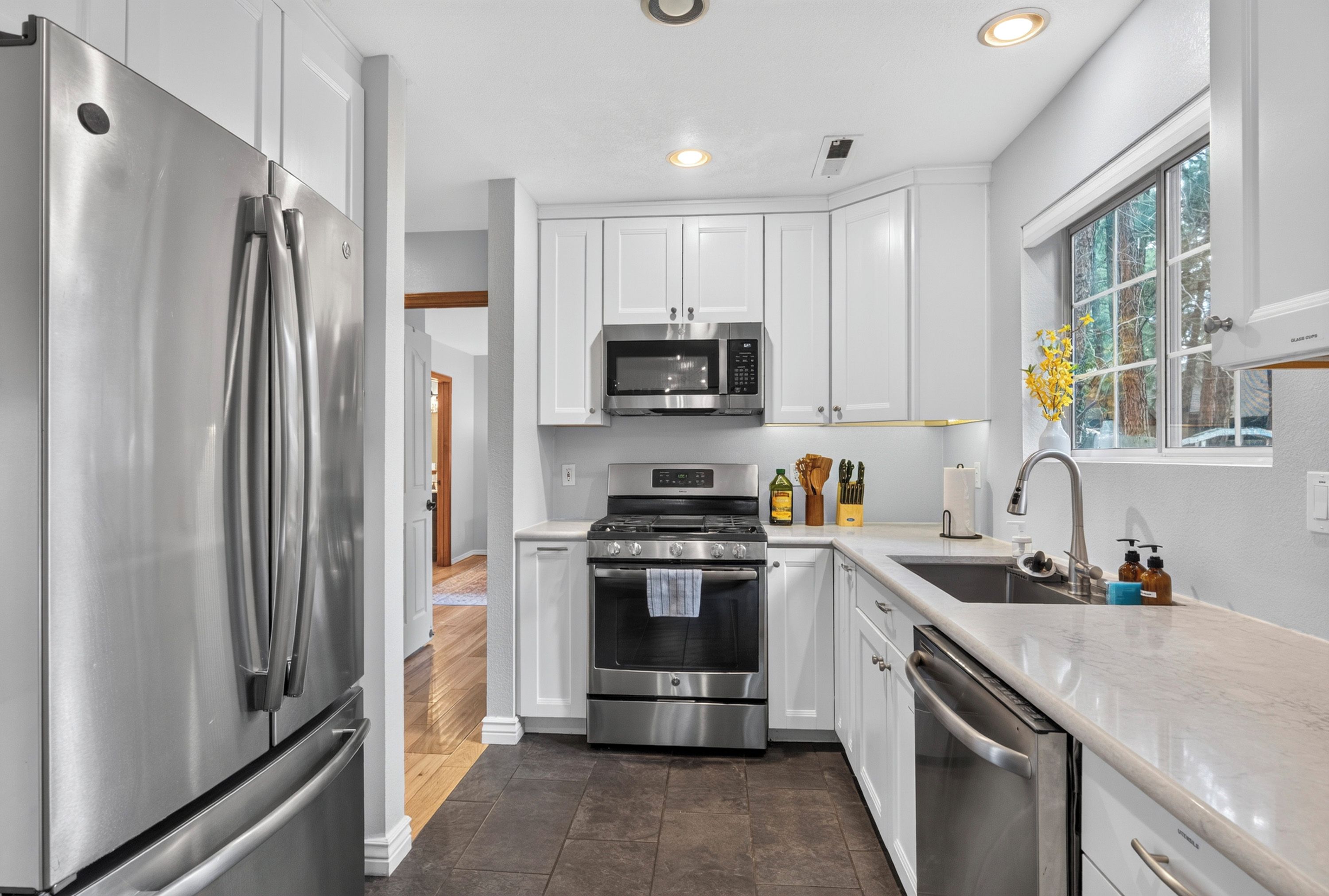 A modern kitchen with stainless steel appliances, white cabinetry, and a window with a view.