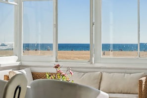 A room with a large window overlooking a beach, a sofa, and a small table with a vase of flowers.
