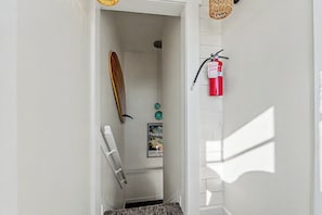 A hallway with a surfboard, a fire extinguisher, and a framed picture on the wall.