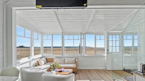 Ein geräumiges Zimmer mit großen Fenstern, einem Sofa, einem Esstisch und einem Fernseher.