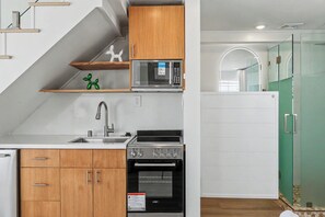 A compact kitchen with wooden cabinets, a stainless steel sink, a microwave, and a built-in oven.