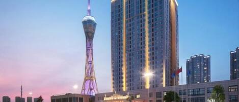 A high-rise building with a distinctive tower structure, a modern hotel with a flat facade, and a clear sky.