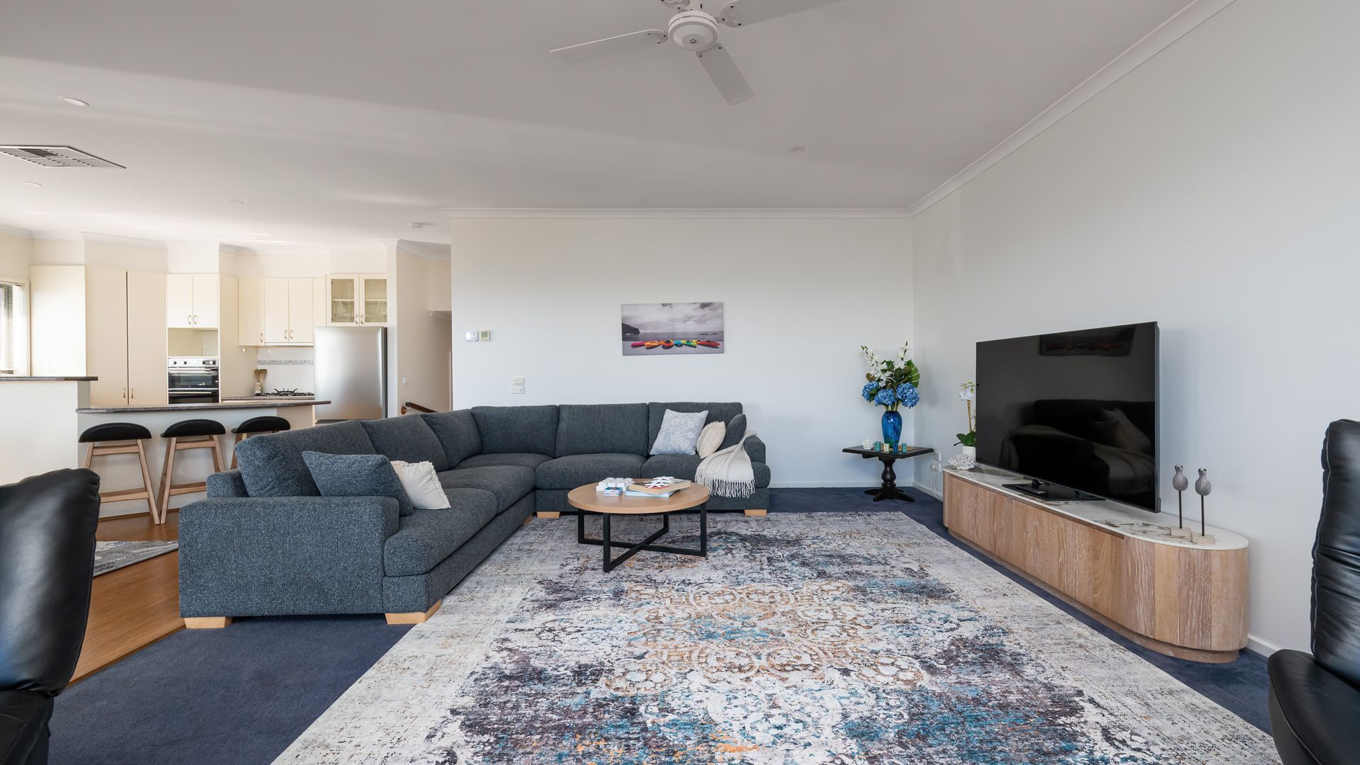 A modern living room with a sectional sofa, a coffee table, a TV, and a kitchen in the background.