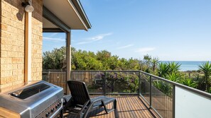 A balcony with a grill, a chair, and a view of the ocean.