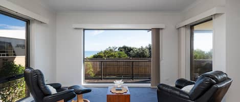 Una sala de estar moderna con balcón, sofás de cuero, una mesa de centro de madera y vista al mar.