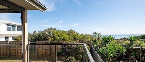 A modern deck with a glass enclosure, overlooking a lush garden and a coastal view.