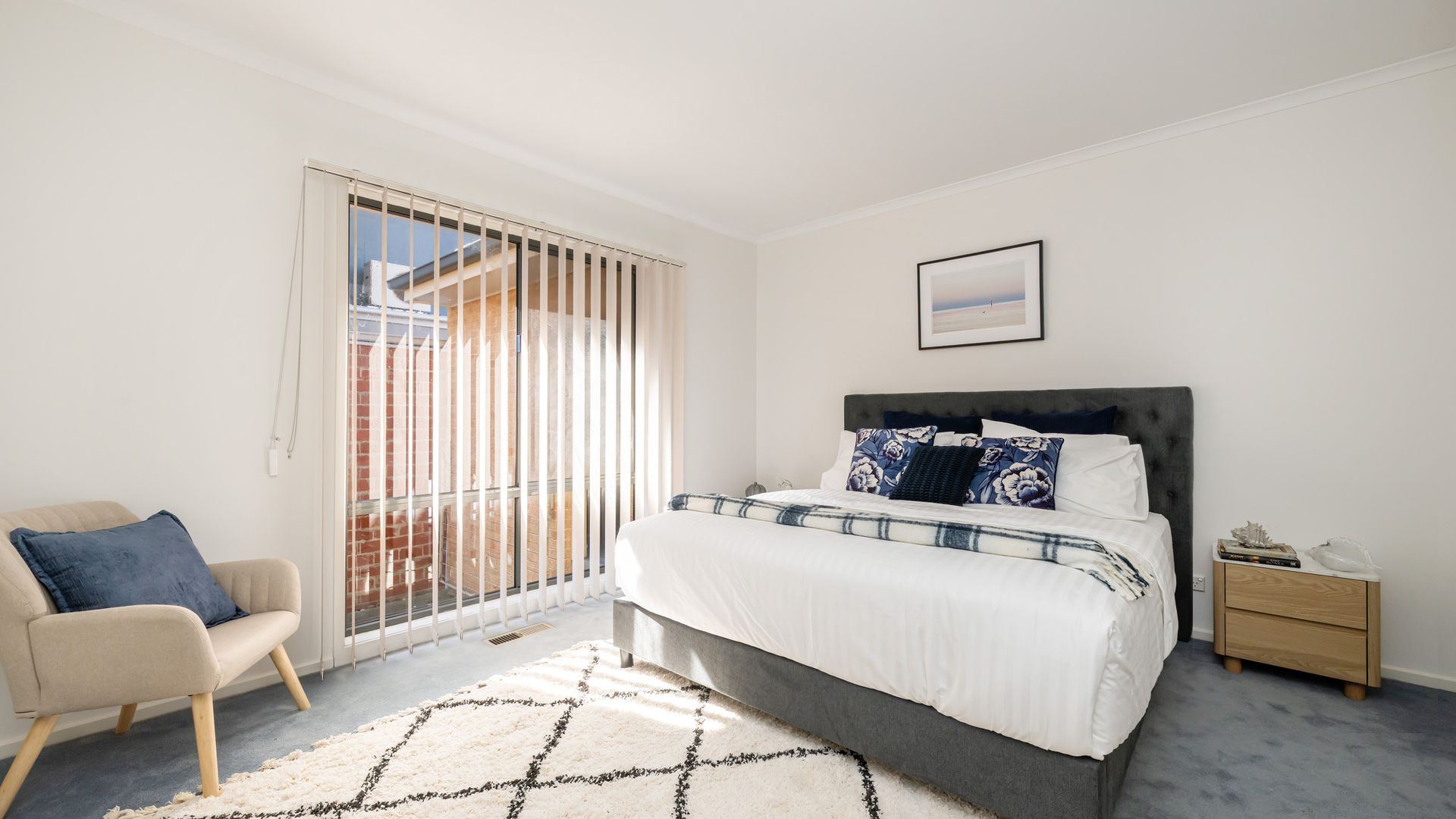 A bedroom with a bed, a chair, a nightstand, and a window with blinds.