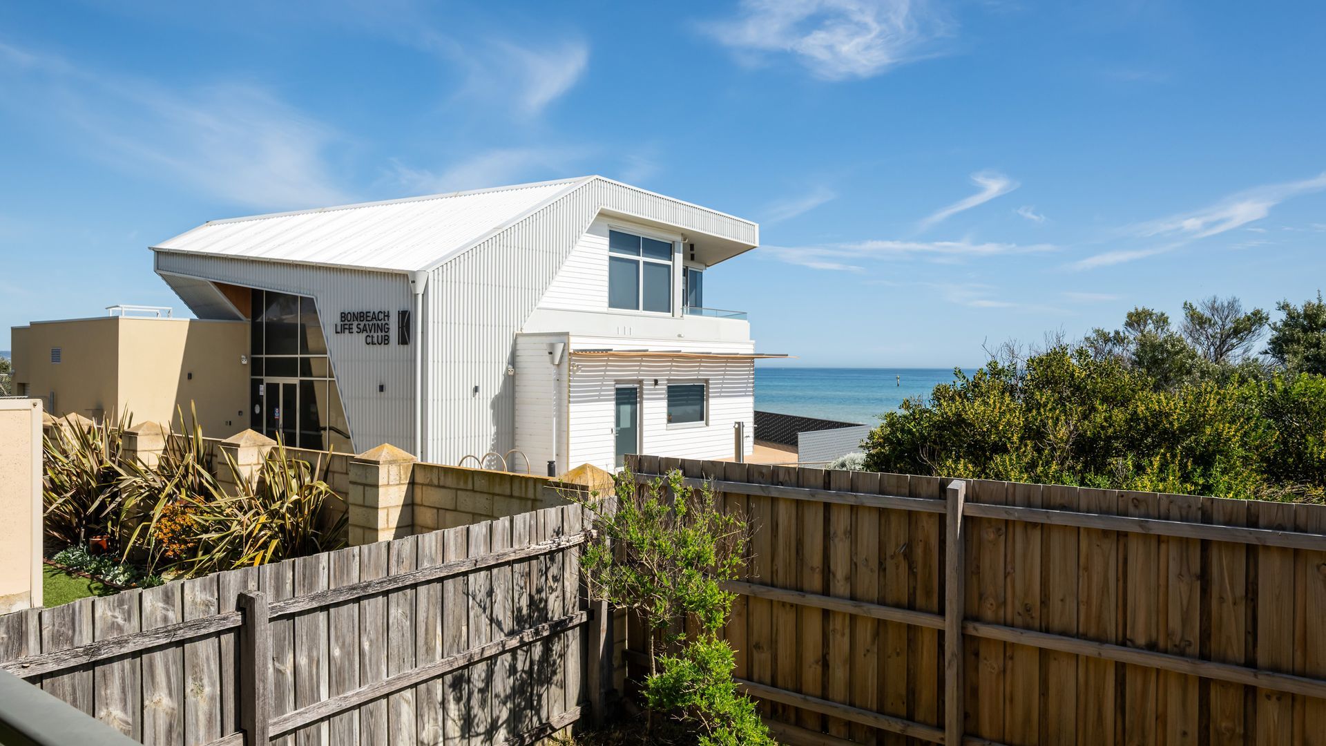 A modern white building with a balcony, a wooden fence, and a view of the ocean.