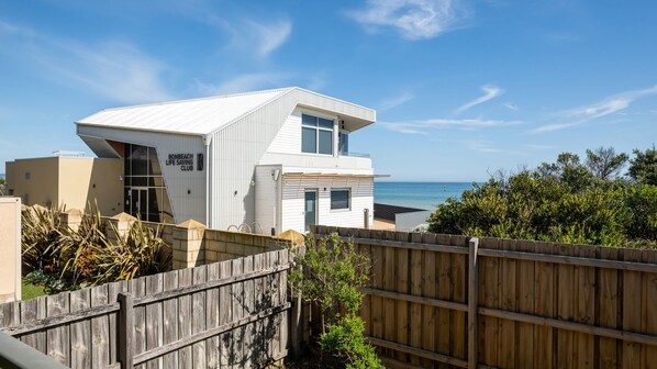 A modern white building with a balcony, a wooden fence, and a view of the ocean.