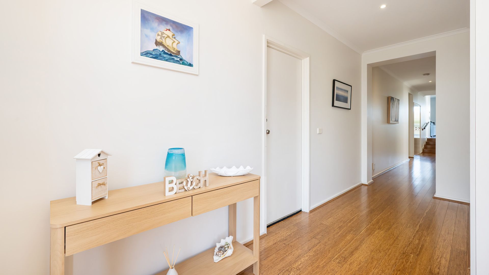 A hallway with a wooden console table, a framed picture, and a door leading to another room.