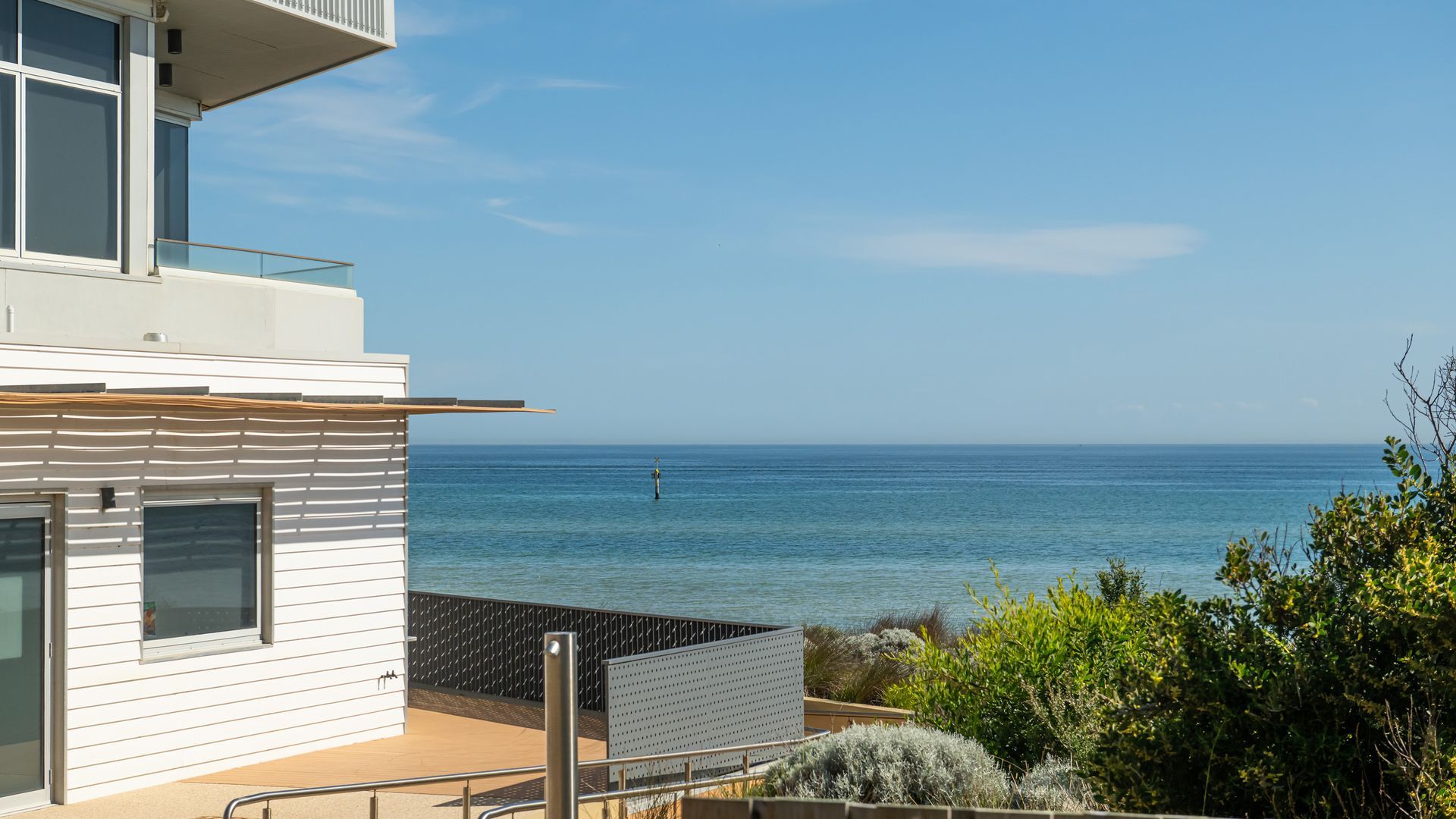 A modern building with a balcony overlooking a clear blue sea.