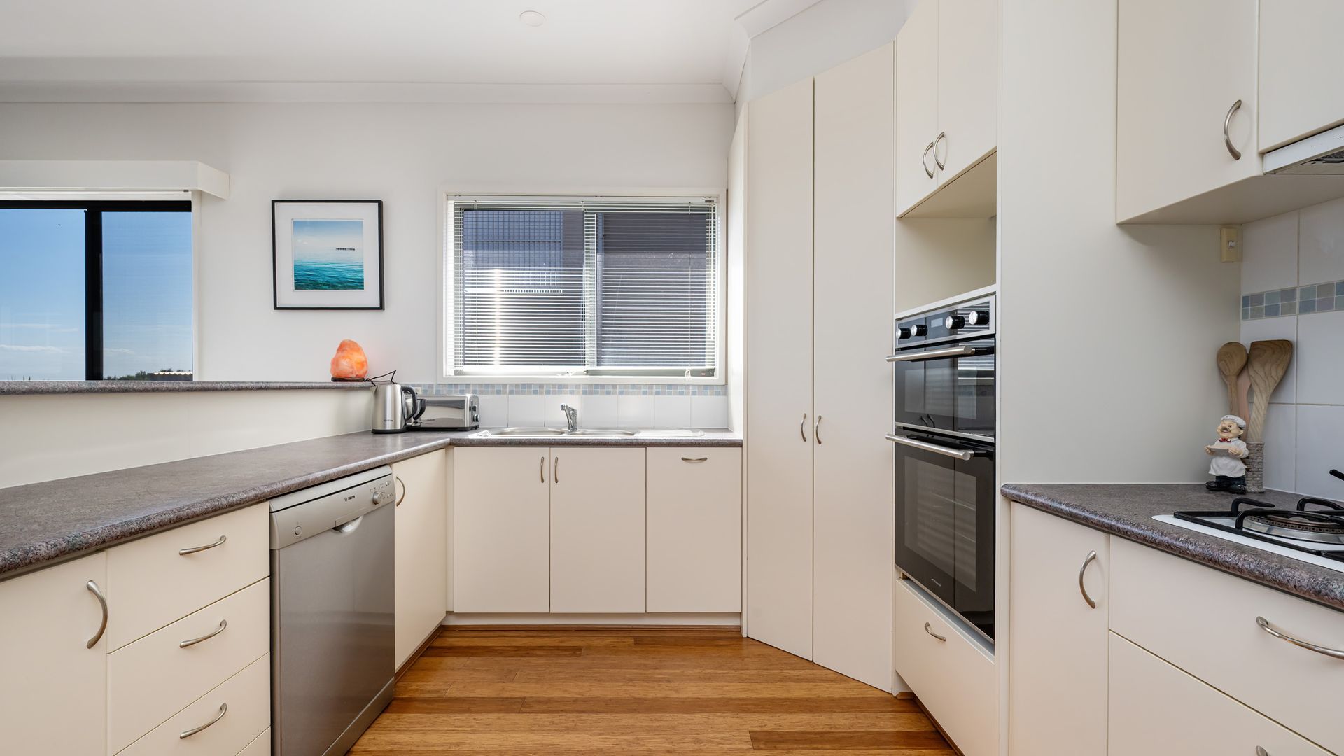 A modern kitchen with white cabinetry, a built-in oven, and a window with blinds.