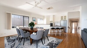 A modern kitchen with white cabinets, a stainless steel refrigerator, and a dining area with a wooden table and grey chairs.