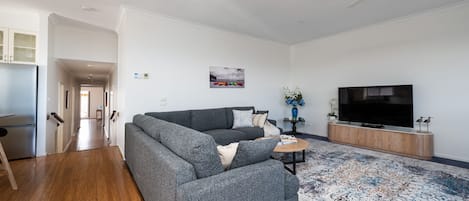 A modern living room with a grey sofa, a flat-screen TV, and a patterned rug.