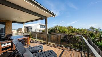 A covered outdoor deck with a table and chairs, a view of a modern building, and a wooden fence.