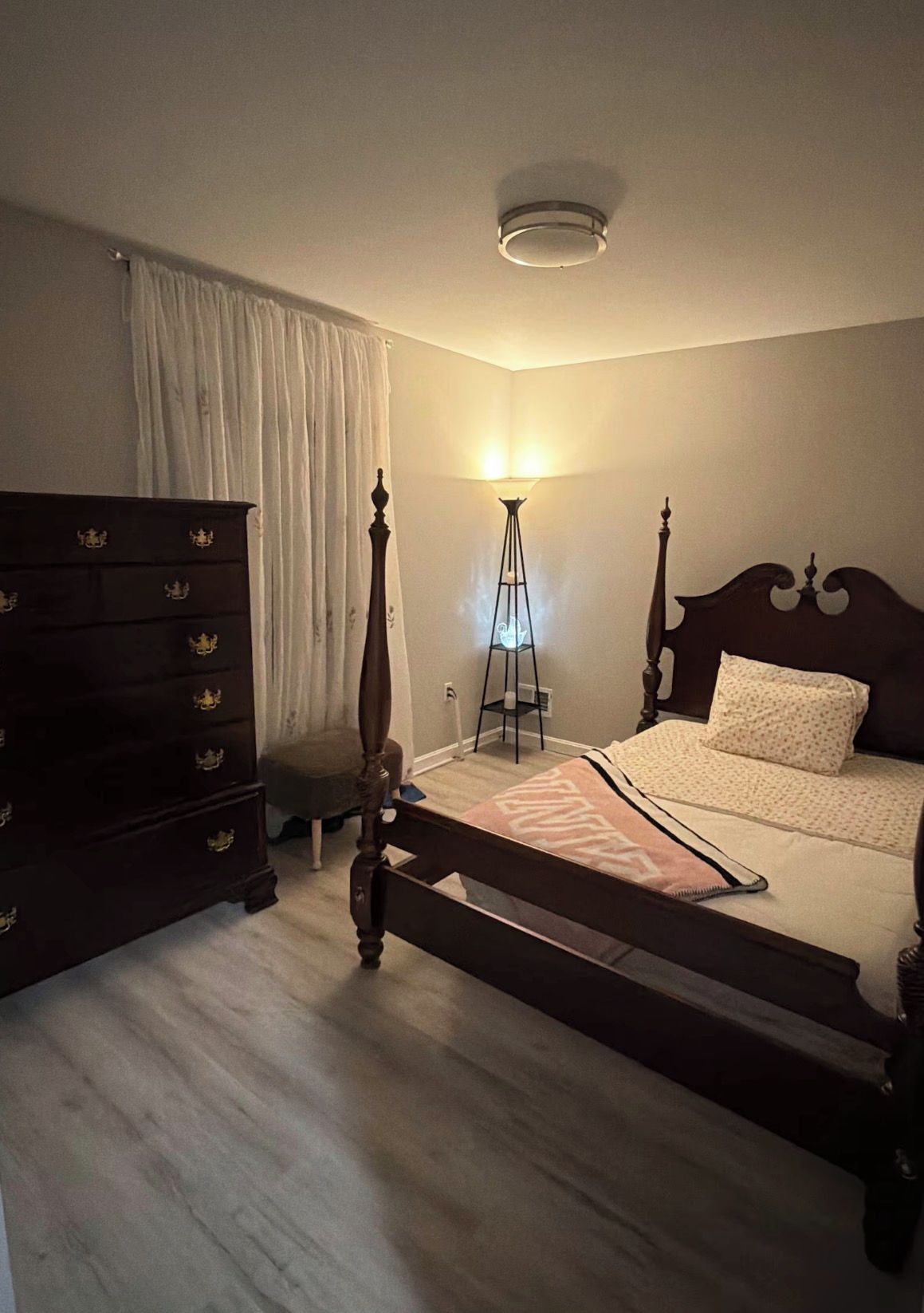 A bedroom with a bed, dresser, and floor lamp.