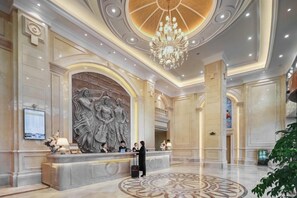 A hotel lobby with a reception desk, a large decorative wall, a chandelier, and a patterned floor. - Vienna International Hotel (Nanjing)