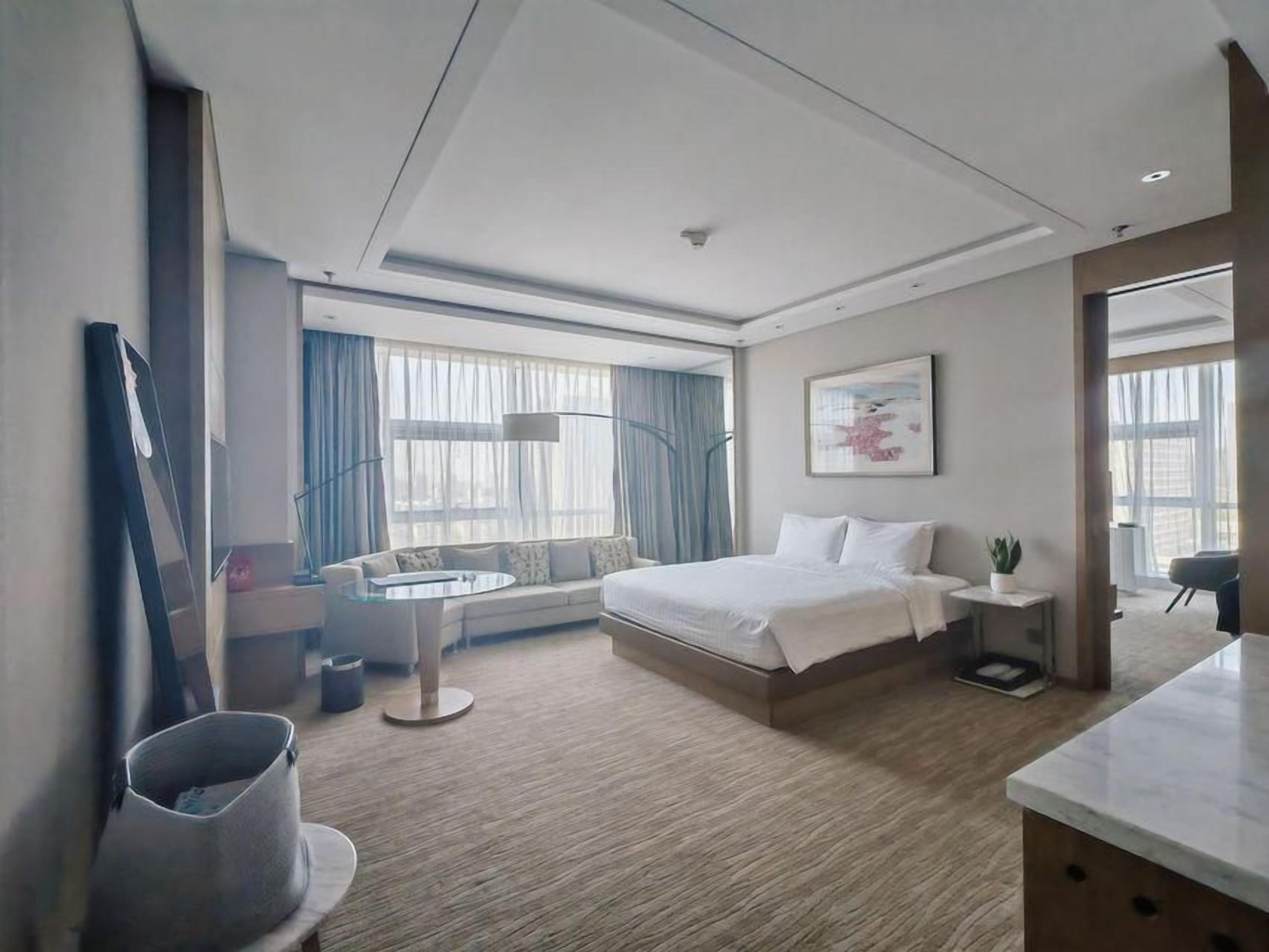 Habitación de hotel moderna con cama, mesita de noche, lámpara y vistas al exterior.