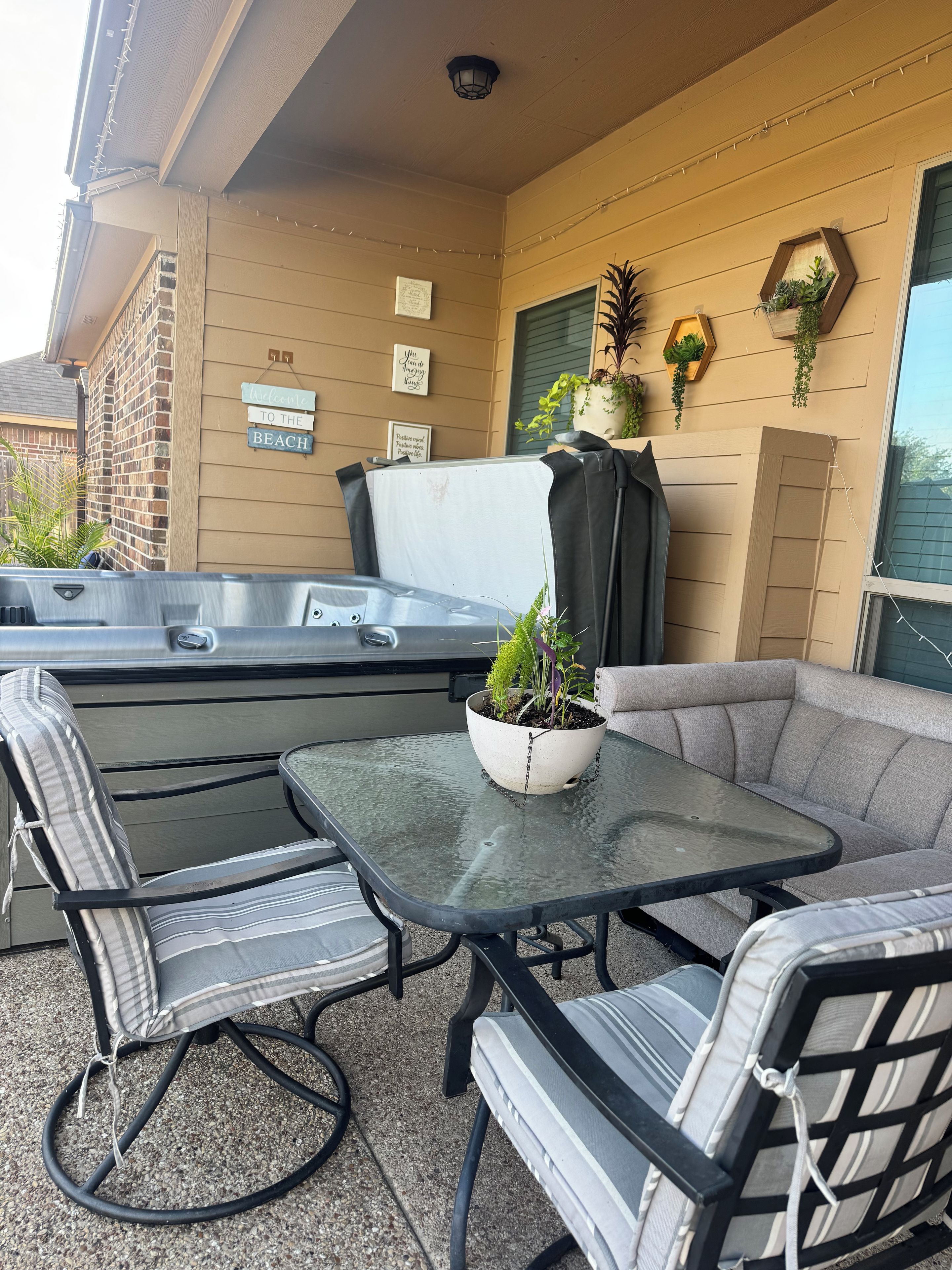Een terras buiten met een glazen tafel, twee gestreepte stoelen, een bank en een jacuzzi.