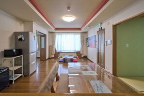 A hotel corridor with a wooden floor, a dining table, a refrigerator, and a green door. - Sapporo Vacation Home B&B (Sapporo)