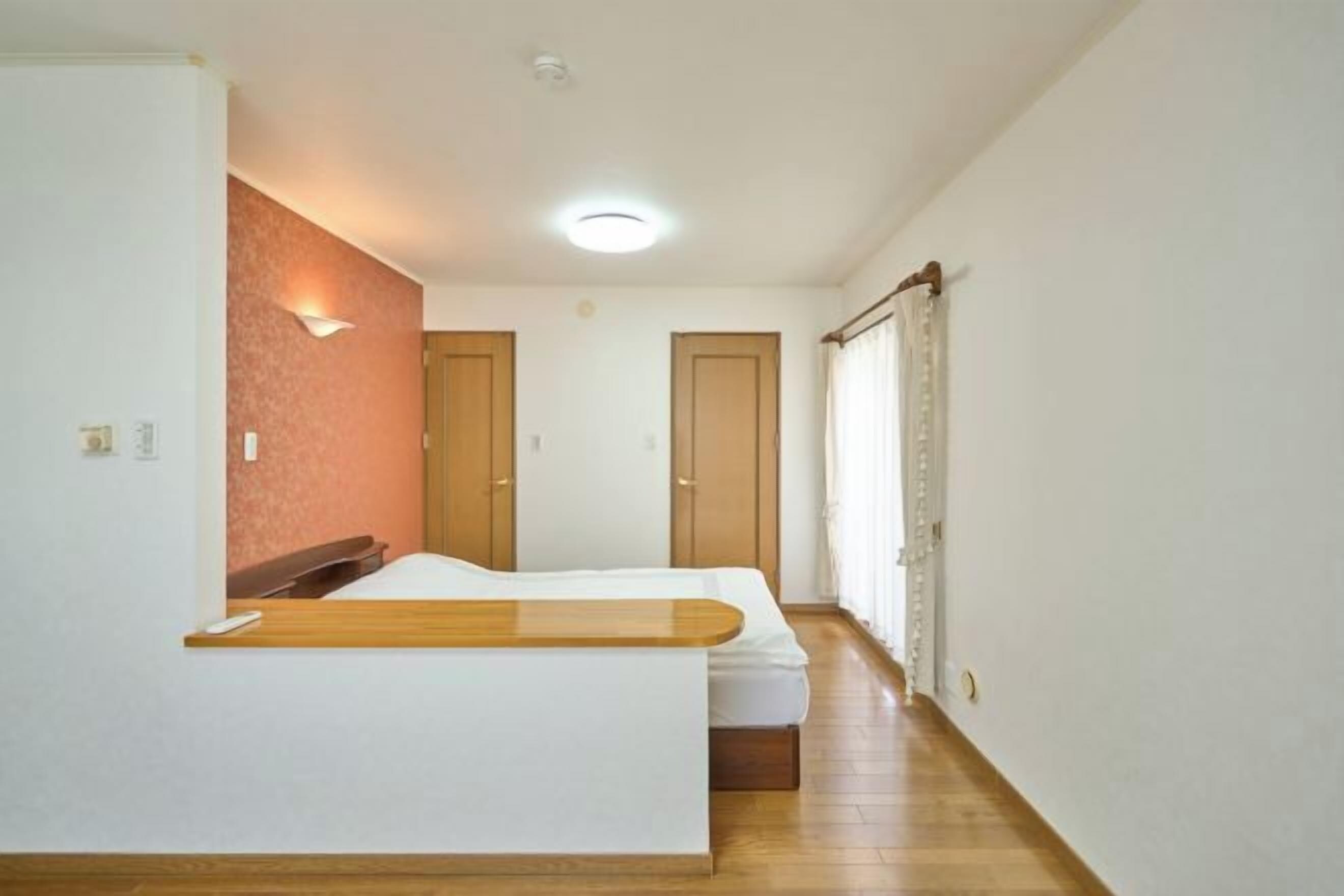 A room with a bed, a wooden bench, a wall-mounted light, and a door.