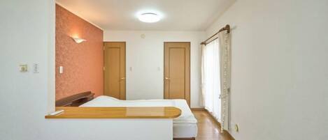 A room with a bed, a wooden bench, a wall-mounted light, and a door.
