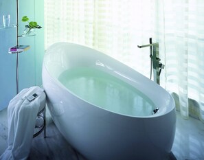 A modern bathroom with a freestanding bathtub, a glass shower enclosure, and a towel rack with a book. - Lavande Hotel (Dongguan)