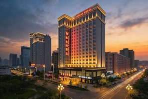 A multi-story hotel with illuminated signage, surrounded by urban buildings and a busy street. - Vienna Hotel (Dongguan)