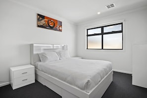 A modern bedroom with a large bed, a bedside table, a window, and a wall-mounted artwork. - Family 5-Bed House Near Tarneit Central (Tarneit)
