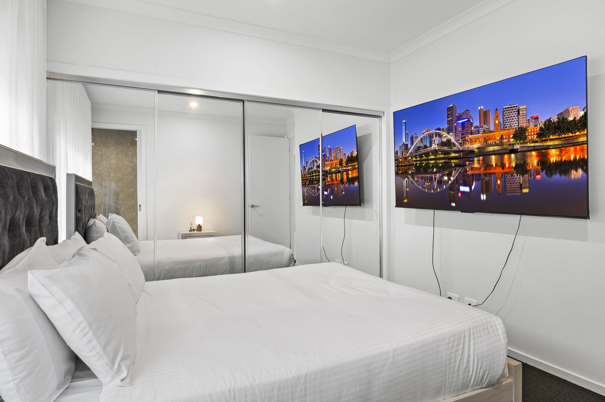 A hotel room with a bed, a nightstand, a mirror, and a large cityscape painting on the wall.