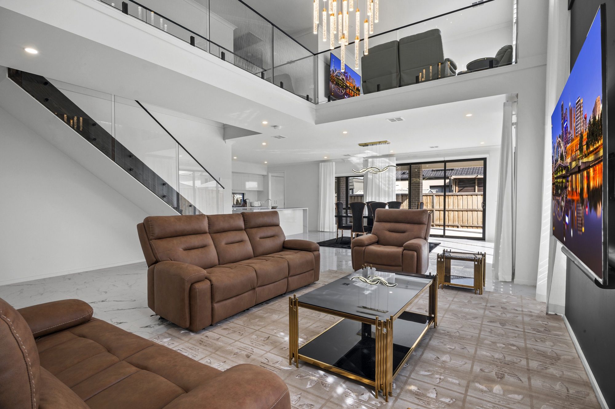 A spacious living area with a high ceiling, a staircase, and a large window with a cityscape view.