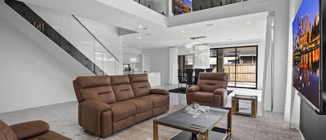 A spacious living area with a high ceiling, a staircase, and a large window with a cityscape view.
