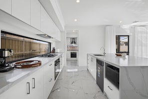 Een moderne keuken met witte kasten, een marmeren vloer en uitzicht naar buiten.