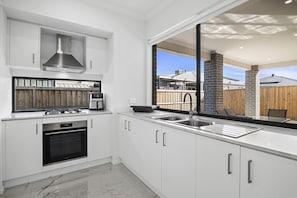 A modern kitchen with a gas stove, oven, and a coffee maker. - Family 5-Bed House Near Tarneit Central (Tarneit)