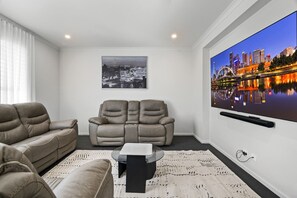Ein modernes Wohnzimmer mit einem Flachbildfernseher, zwei Sofas, einem Couchtisch und einem gerahmten Stadtbild an der Wand.