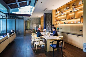 A modern restaurant interior with a long counter, wooden shelves with items, and a seating area with chairs and tables. - Yaoxi Dynasty Hotel (Wenzhou)