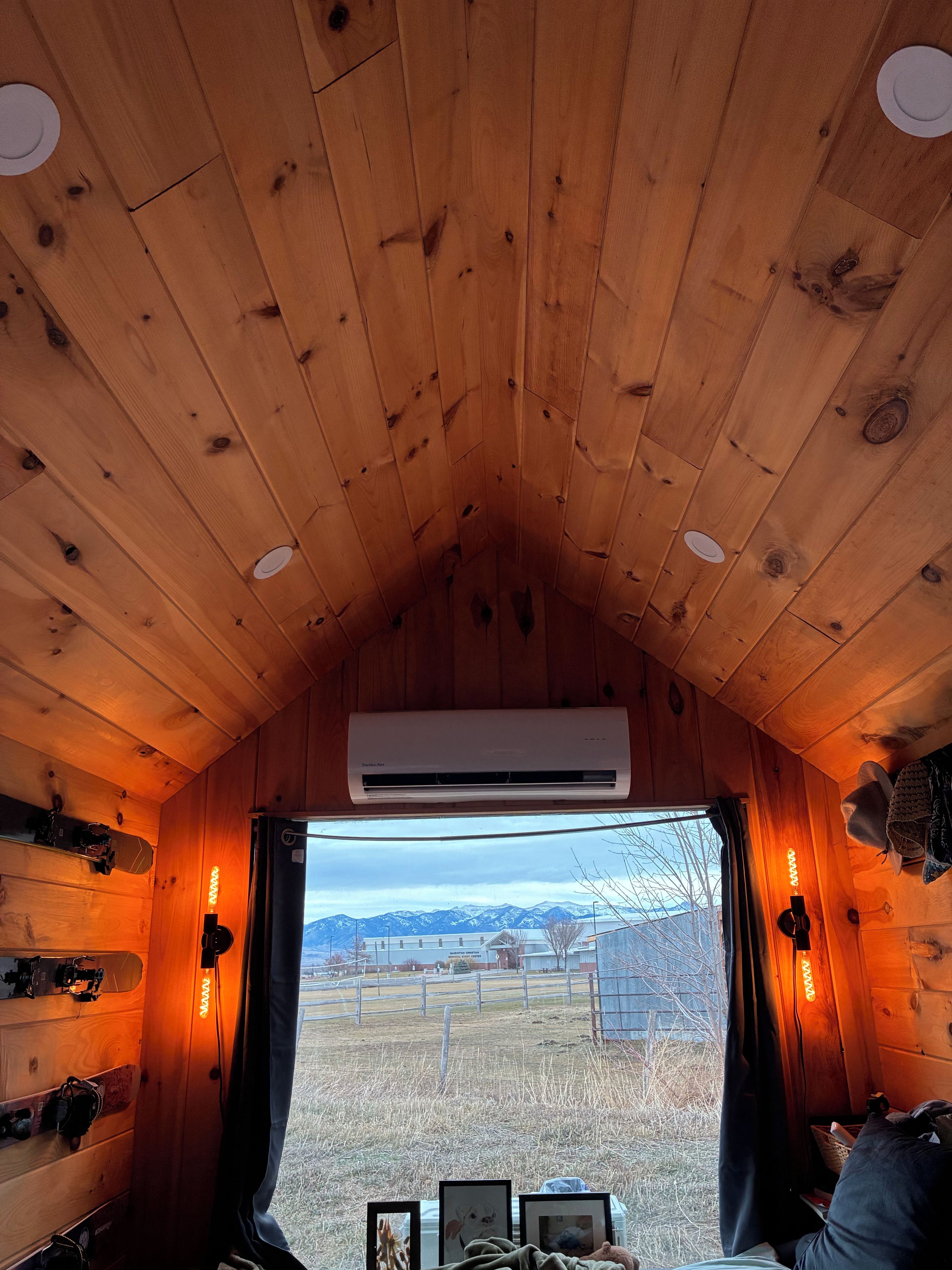 Interno di una baita con pareti in legno, soffitto spiovente, condizionatore, finestra con tende e vista su un paesaggio innevato.