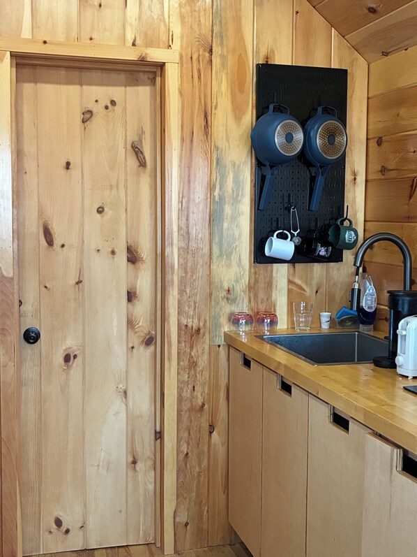 Un interior de madera con una cocina que incluye un lavamanos, una cafetera y un hervidor.