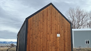 A wooden building with a black roof, a small porch, and a metal fence.