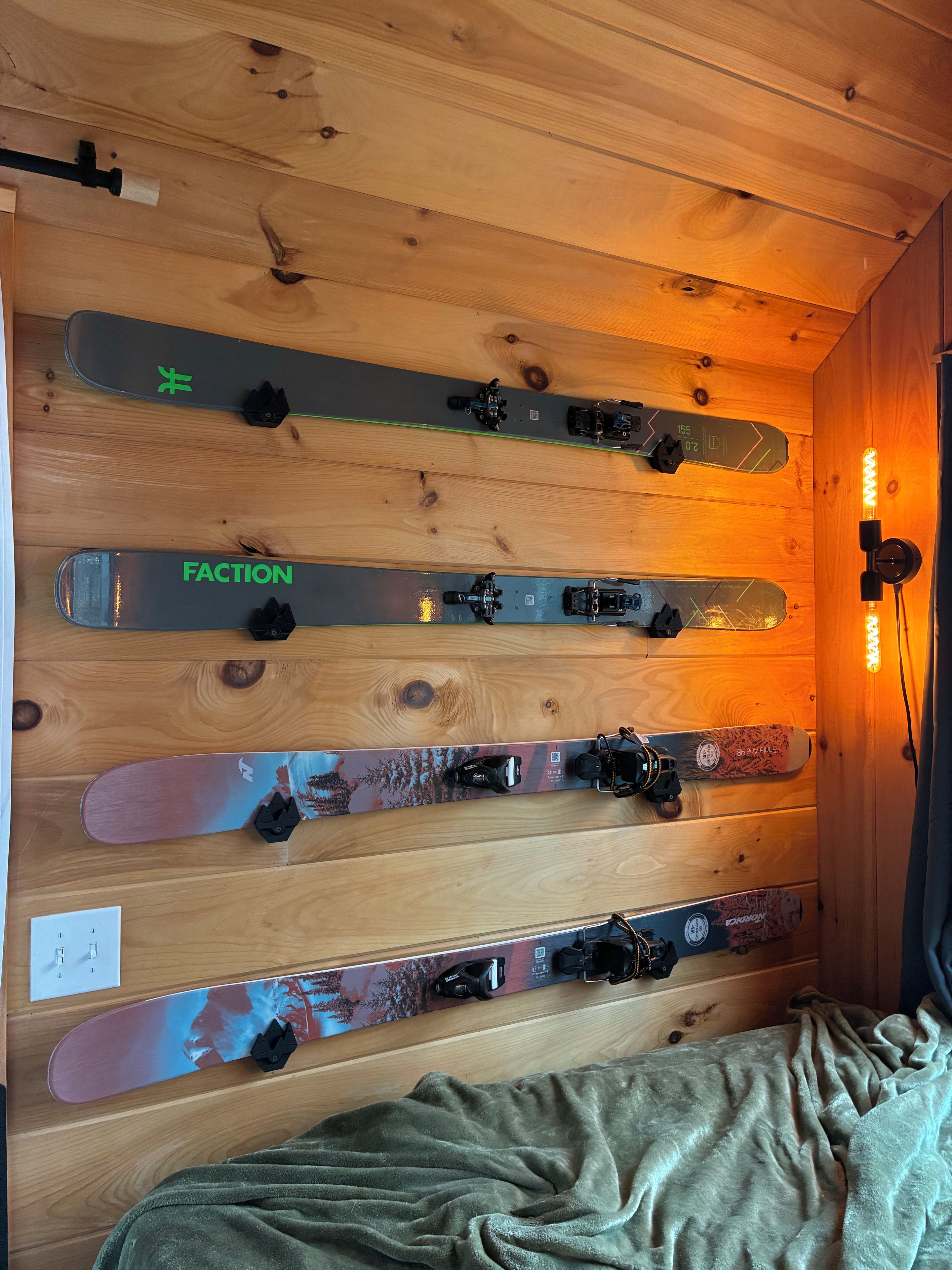 Une pièce aux murs en bois, avec un lit. Plusieurs paires de skis et de snowboards sont accrochées au mur.
