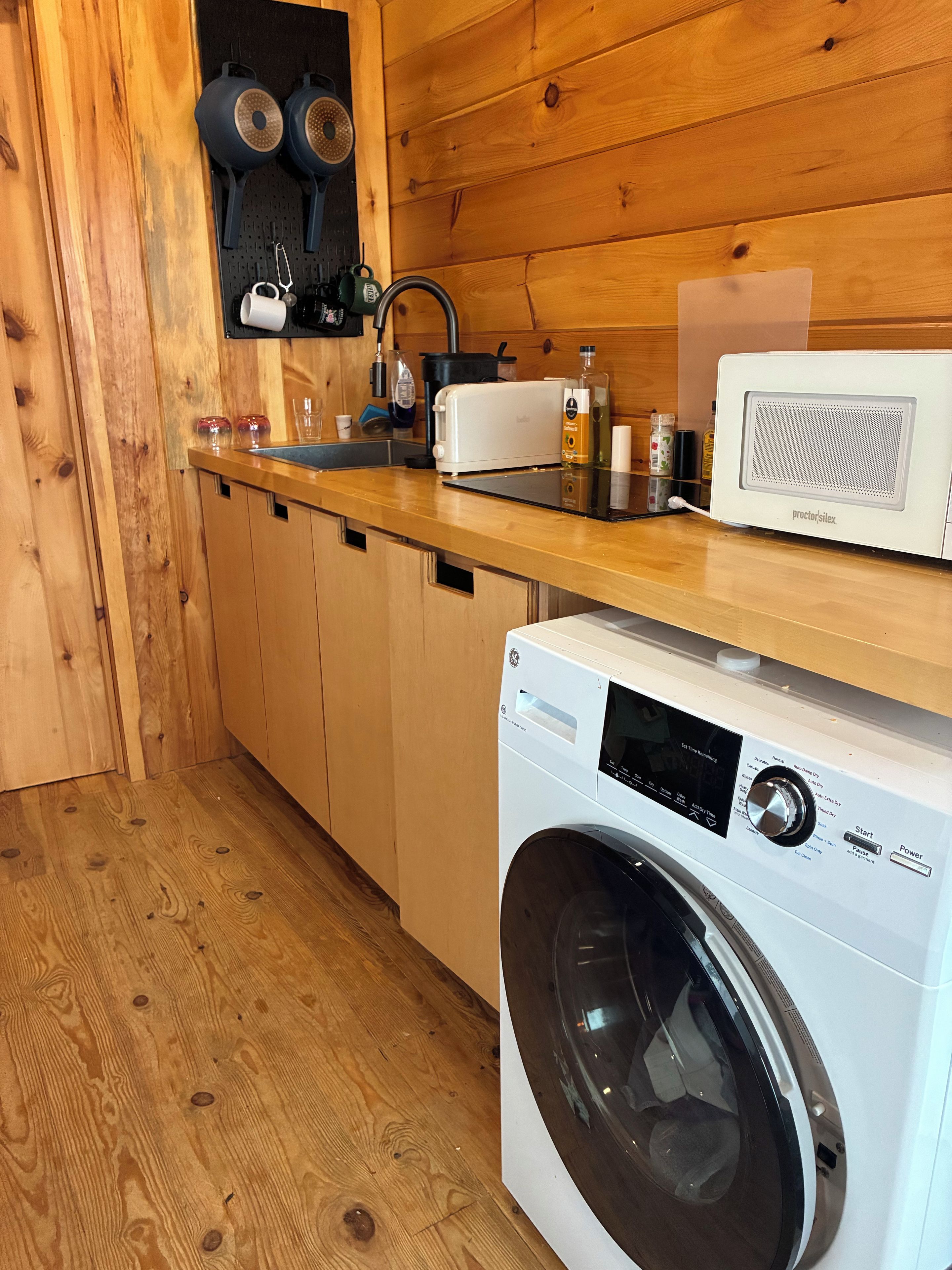 Une cuisine de taille réduite, dotée de meubles en bois, d’un lave-linge, d’un four à micro-ondes et d’un évier.
