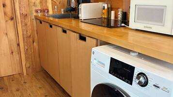 Une cuisine de taille réduite, dotée de meubles en bois, d’un lave-linge, d’un four à micro-ondes et d’un évier.