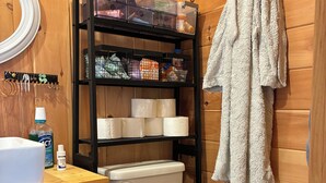 A wooden bathroom with a toilet, a shelf with toiletries, and a towel hanging on the wall.
