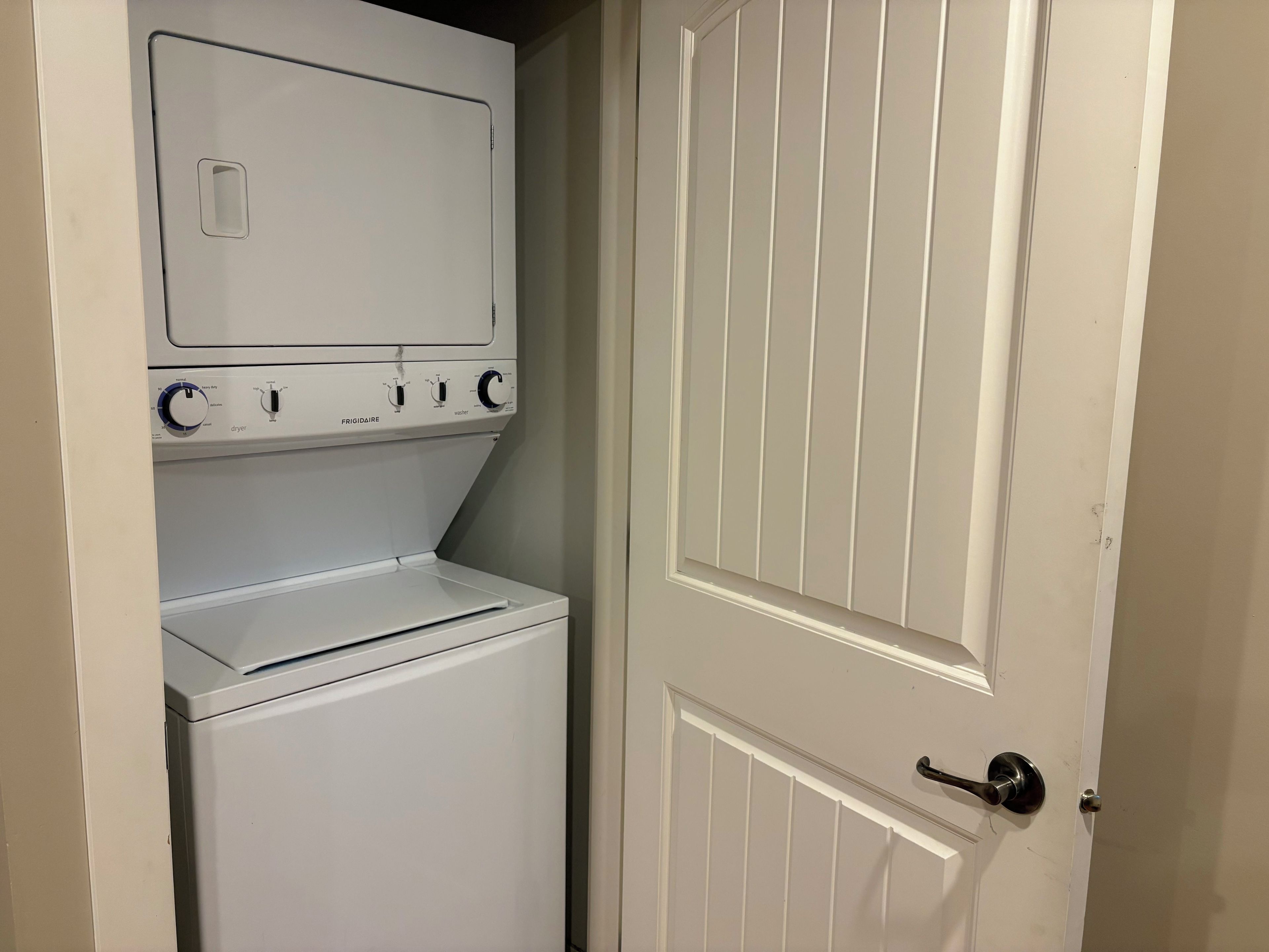 A laundry room with a front-loading washer and dryer, a door with a handle, and a white wall.
