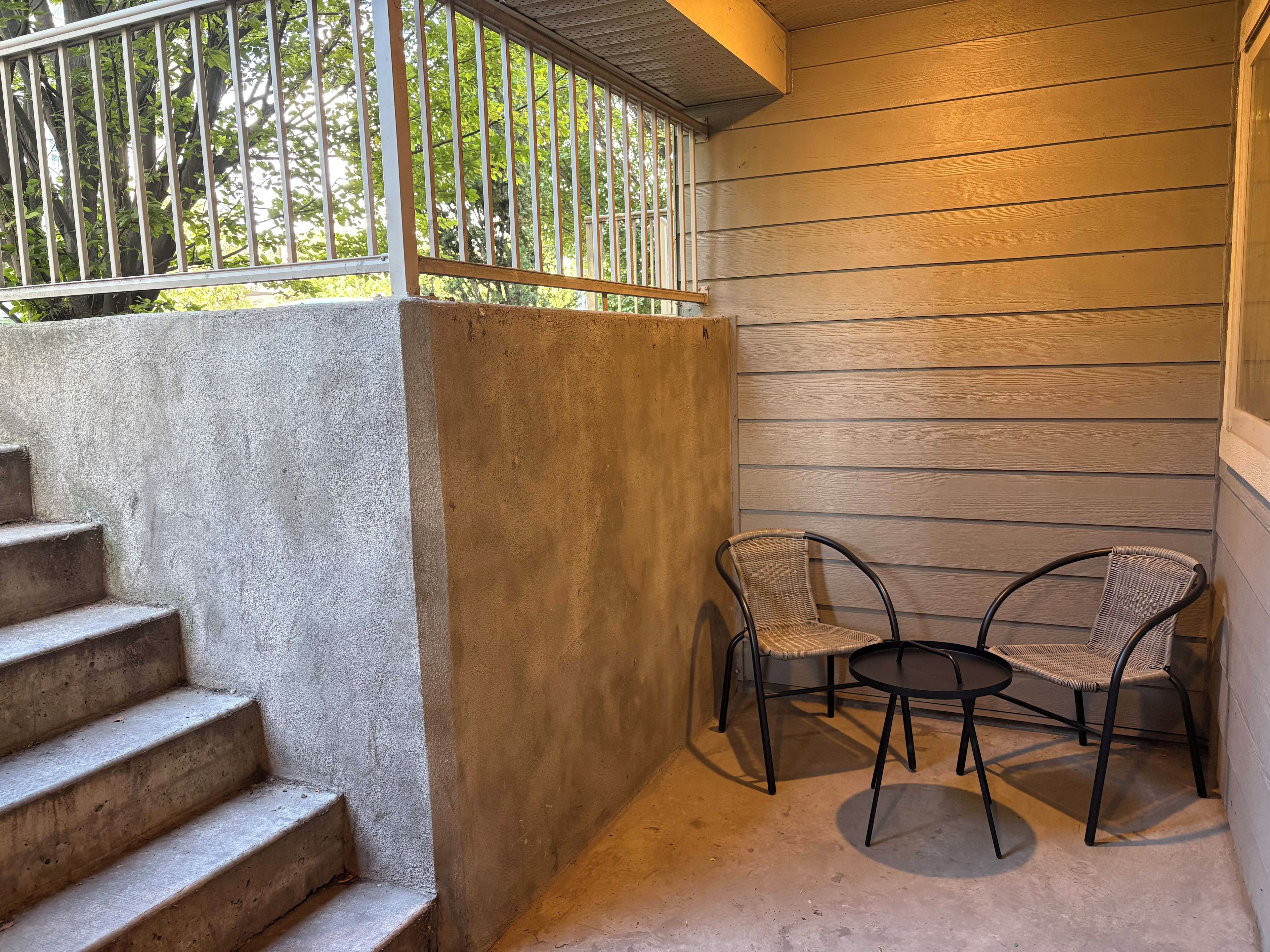 A covered outdoor area with a concrete staircase, two wicker chairs, and a small round table.