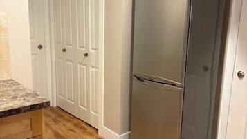 A kitchen with wooden flooring, a stainless steel refrigerator, and white double doors.
