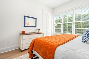 A bedroom with a bed, dresser, mirror, and large window.
