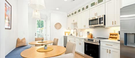 A modern kitchen with white cabinetry, stainless steel appliances, and a dining area with a round table and chairs.