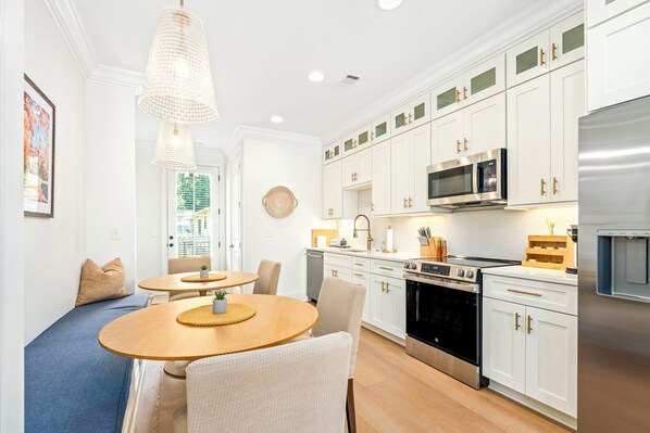 A modern kitchen with white cabinetry, stainless steel appliances, and a dining area with a round table and chairs.