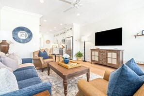 A modern living room with a sofa set, a coffee table, a television, and a kitchen area in the background.